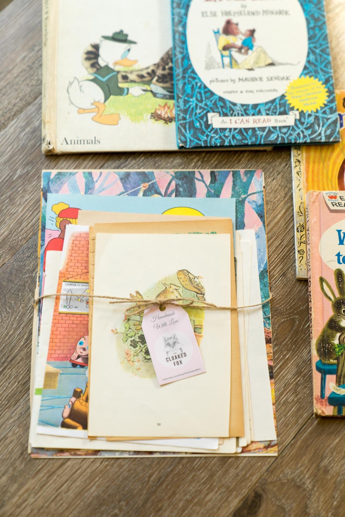 Styled flat lay of illustrated vintage children’s book pages arranged on a hardwood surface with additional vintage books for a cozy, nostalgic look.