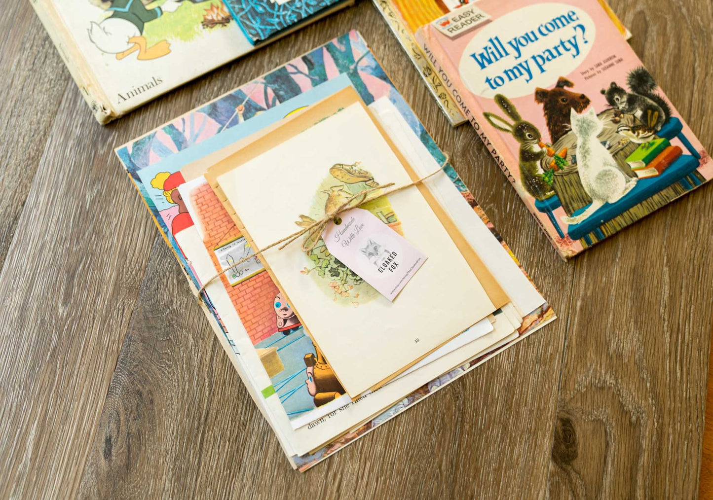Styled flat lay of illustrated vintage children’s book pages arranged on a hardwood surface with additional vintage books for a cozy, nostalgic look.