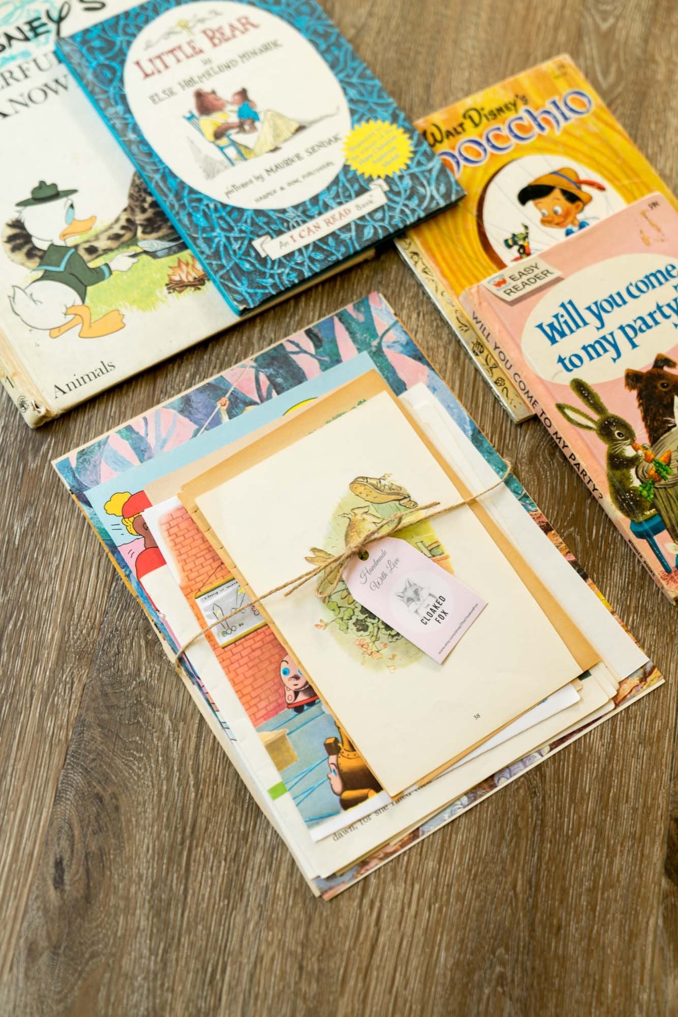 Top-down image of assorted vintage children’s storybook pages with aged edges and illustrations, styled with hardcover books on a wood surface.