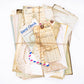 Flat lay of coffee-dyed vintage paper ephemera including ledger sheets, book pages, and tickets on a rustic background
